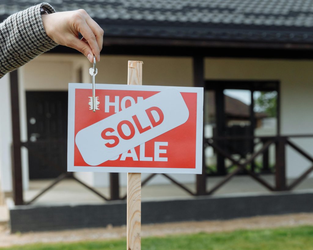 A hand holding a key, and a sold signage in front of a house. Selling Your Home in Corona, CA: Tips for a Quick and Successful Sale